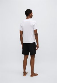 Camiseta blanca de manga corta y pantalones cortos negros, tela suave, ajuste relajado, diseño sencillo, sin patrones ni acentos visibles, pies descalzos.