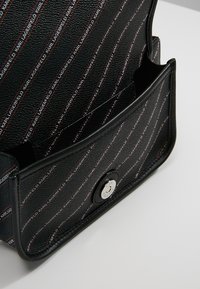 Borsa in pelle nera con design piatto. L'interno presenta una fodera a motivo con testo ripetuto. Dettaglio di chiusura a scatto magnetico sulla parte anteriore.