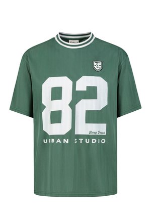 Green short-sleeve shirt with white striped round collar, large white number 82, and text "Urban Studio" and "Deep Focus" on front.