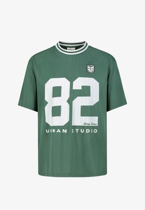 Grünes kurzärmeliges Hemd mit weiß gestreiftem Rundkragen, großer weißer Zahl 82 und Text "Urban Studio" und "Deep Focus" auf der Vorderseite.