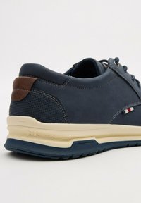 Zapatilla de color azul marino con un upper de textura suave, acento de cuero marrón, lado perforado y una suela de color crema con un agarre estampado.