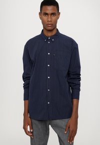 Marineblauwe gestreepte button-up shirt met een puntige kraag, lange mouwen en een borstzak. De stof heeft een zachte textuur met een subtiele glans.