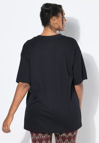 Zwarte oversized t-shirt met korte mouwen, ronde halslijn en een gladde textuur. Draag het met gestreepte, aansluitende broek met ingewikkelde ontwerpen.