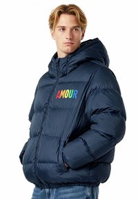 Doudoune bleu marine avec capuche, ornée d'une broderie arc-en-ciel "AMOUR" sur la poitrine et de poignets élastiques ; texture lisse et brillante.