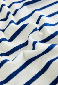 Baumwollstoff mit weißem Hintergrund und marineblauen horizontalen Streifen, zeigt eine weiche Textur und leichte Faltenbildung.