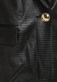 Tissu en similicuir noir texturé avec un motif reptile, orné d'un bouton doré et d'un détail poche sur le côté.