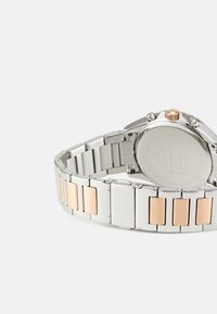 Reloj de metal plateado y oro rosado con pulsera de eslabones, que presenta acentos pulidos y una corona texturizada; caja redonda con un dorso liso.