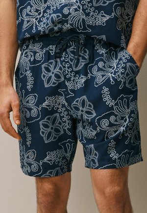Navy blue shorts with white floral embroidery, elastic waistband with drawstring, worn with a matching embroidered shirt.