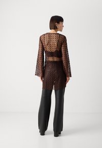 Lace top in dark brown with a patterned design, featuring long bell sleeves and a backless cut, paired with black leather pants.