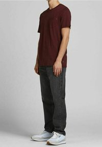 Mörkröd t-shirt med korta ärmar och bröstficka, kombinerad med mörkgrå jeans och vita sneakers med grå och bruna detaljer.