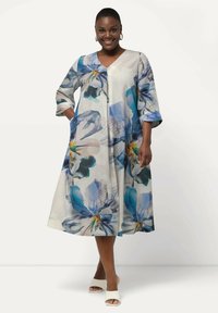 Vestido de estampado floral con mangas tres cuartos, escote en forma de V y bolsillos. Tejido ligero con patrones florales en azul, verde y amarillo sobre un fondo blanco.