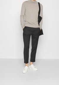 Pull en tricot col roulé gris, pantalon noir fuselé et baskets blanches. Détails notables : design épuré, poignets roulés et textures lisses.