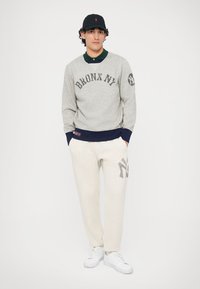 Gray sweatshirt with "BRONX NY" text, navy cuffs, paired with off-white sweatpants featuring a large “NY” design, and white sneakers.