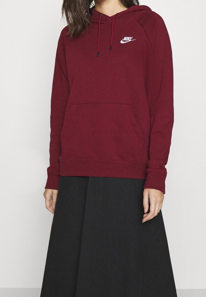 Bordeaux hoodie med framficka, långa ärmar, dragsko i huvan och vit Nike-logotyp på bröstet, matchad med en svart kjol.