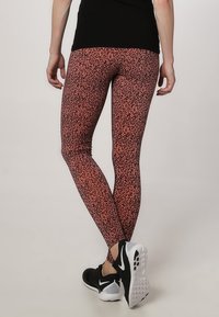 Leggings i ett rosa och svart prickigt mönster, figurnära design, elastiskt material, matchat med svarta träningsskor med vita detaljer.