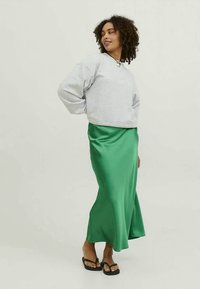 Pelēks džemperis ar garām piedurknēm, kopā ar zaļu satīna garu svārku. Apģērbs ir papildināts ar melniem čībiņām. Redzamas gludas tekstūras.