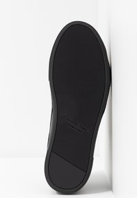 Semelle de chaussure noire en caoutchouc texturé antidérapant, avec étiquette en relief et taille 37. Design plat avec bords lisses et courbure subtile.