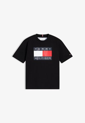 Czarna koszulka z krótkim rękawem, z centralnym logo Tommy Hilfiger przedstawiającym czerwono-białą prostokątną flagę oraz nazwę marki powyżej i poniżej.