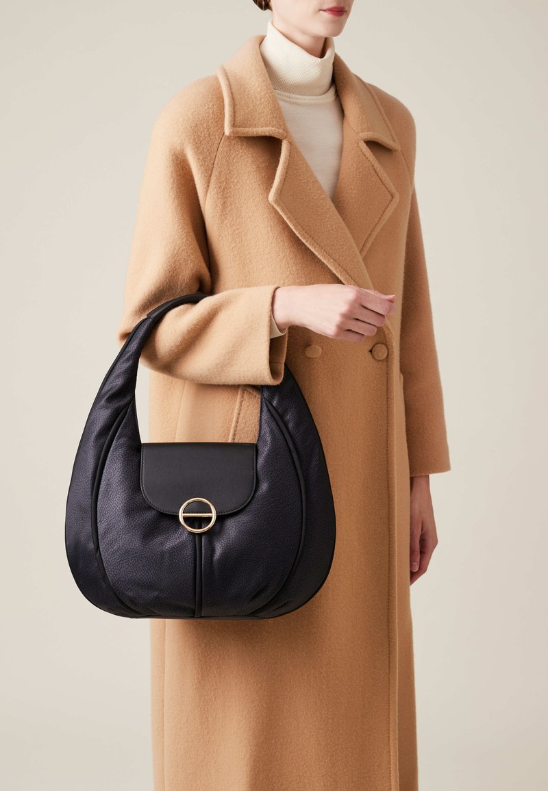 Black leather hobo bag with a rounded silhouette, textured finish, and a front flap featuring a circular gold accent.