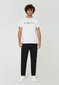 Bílá krátká trička s krátkým rukávem, na kterém je černě vytištěné "SAIL RACING". V kombinaci s černými slim-fit kalhotami a bílými teniskami. Jednoduchý, sportovní design.
