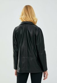 Giubbotto di pelle nera con design aderente, schiena dritta, colletto a bavero e dettagli delle cuciture. Tessuto leggero e dalla superficie liscia.