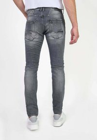 Grijze denim jeans met een slim fit, voorzien van achterzakken en subtiele vervaging. Gecombineerd met witte schoenen, gezien vanaf de achterkant.