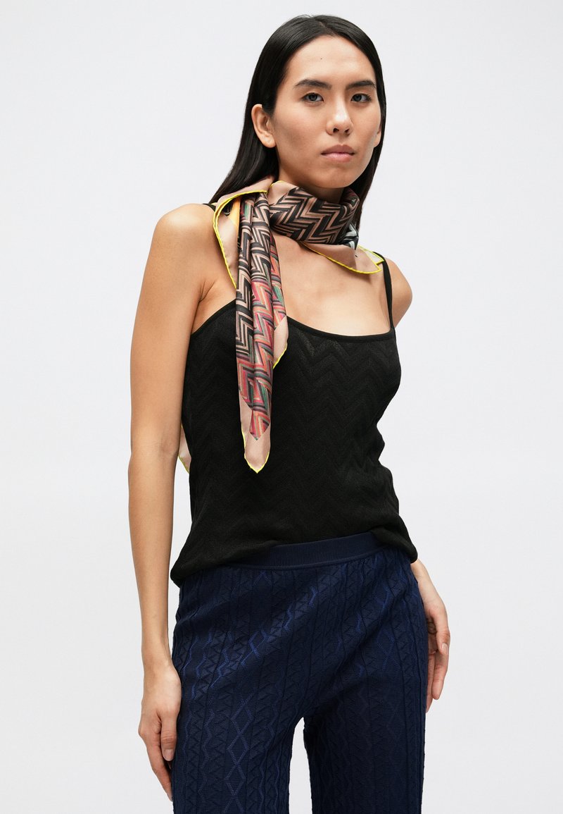 Top nero con texture abbinato a pantaloni blu navy con motivo a fantasia. Un foulard colorato con dettagli gialli è annodato intorno al collo.