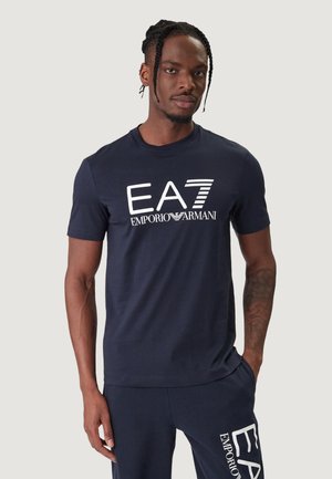 T-shirt in cotone blu navy con scritta bianca "EA7 EMPORIO ARMANI" sul davanti. Maniche corte e scollo rotondo classico.