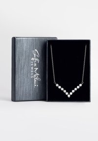 S�ølv halskæde med runde funklende sten arrangeret i en V-form, vist i en sort fløjlskasse med en metalgrå ydre.