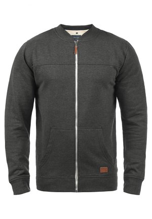 Sudadera gris con cremallera hecha de forro polar texturizado, con cuello redondo, dos bolsillos frontales y un parche de logo marrón en el dobladillo.