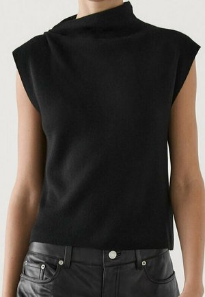 Haut noir sans manches à col montant porté avec un pantalon en cuir noir, montrant le torse supérieur et les bras sur un fond uni.