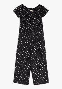 Combinaison à pois noirs avec un corsage smocké, des manches courtes et des pantalons évasés. Fabriquée en tissu léger, avec des pois blancs.