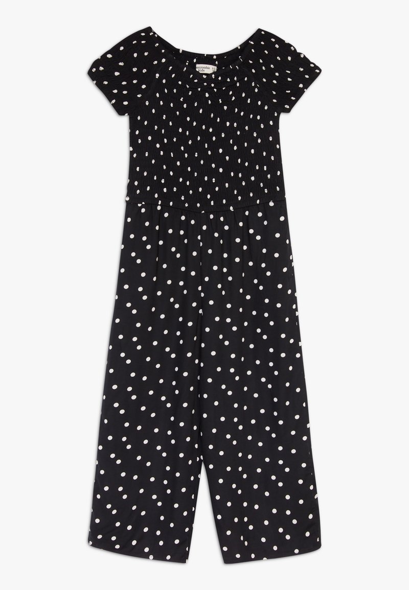 Combinaison à pois noirs avec un corsage smocké, des manches courtes et des pantalons évasés. Fabriquée en tissu léger, avec des pois blancs.