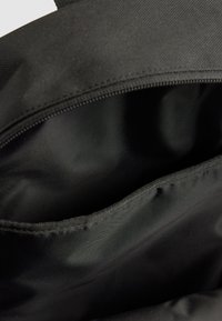 Zwarte stoffen tas interieur met een open ritsvak, voorzien van een gladde, iets reflecterende voering en een gestructureerd buitenmateriaal.