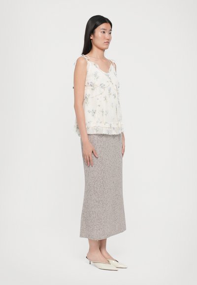 Top din material ușor, cu un model floral, cu volane și bretele subțiri, asortat cu o fustă texturată bej, până la genunchi, și încălțăminte albă tip slip-on.