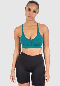 Teal ribbattu bralette dengan bagian depan berkerut dan tali tipis, dipadukan dengan celana pendek bersepeda hitam tinggi. Tekstur yang halus dengan pas yang pas.