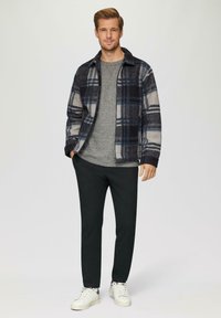 Veste en flanelle à carreaux bleu marine, gris et crème avec un col; pull gris en dessous; pantalon noir; baskets blanches.