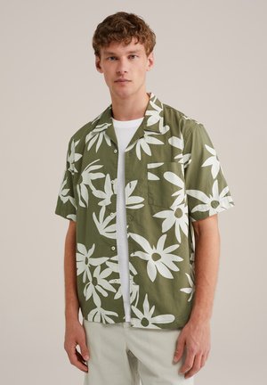 Camisa de manga corta verde oliva con patrón floral blanco, un bolsillo en el pecho y cierre de botones. Tela suave con un corte holgado.