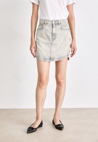 Denim mini-jurk in een lichte wassing, met een hoge taille, voorzakken en een zoom met lichte slijtage. Gecombineerd met zwarte puntige ballerina's.