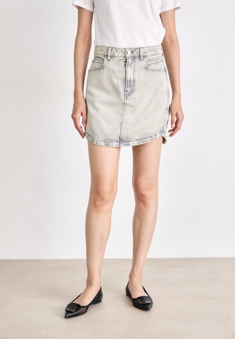 Denim mini-jurk in een lichte wassing, met een hoge taille, voorzakken en een zoom met lichte slijtage. Gecombineerd met zwarte puntige ballerina's.