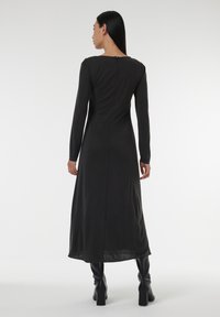 Robe noire à manches longues avec fermeture éclair au dos, présentant une texture lisse et un corsage ajusté qui s'évase vers l'ourlet.