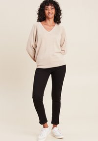 Beige gebreide trui met een V-hals, losse mouwen en glans. Gepaard met strakke zwarte broek en witte sneakers. Eenvoudig en modern ontwerp.
