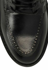 Zwarte leren schoen met een glanzende afwerking, brogue-details met decoratieve metalen studs langs de rand en vetersluiting.
