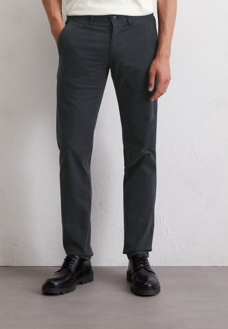 Dunkelgraue Chinos aus Baumwolle mit geradem Bein, Fronttaschen und kombiniert mit schwarzen Schnürboots.