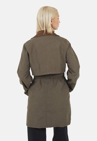 Cappotto trench verde oliva con colletto marrone, vita cinturata e maniche lunghe. Presenta un design posteriore a taglio dritto con una finitura texturizzata.