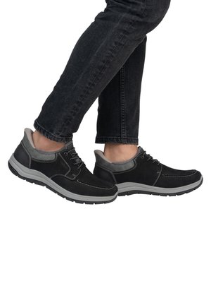 Schwarze Wildlederschuhe mit grauen Akzenten, einem niedrigen Profil, gesteppten Details und einer dicken Gummisohle. Getragen mit dunklen Jeans.