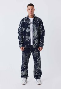 Conjunto de mezclilla en un patrón de cuadros en navy y gris. Camisa de botones y pantalones a juego. Camiseta blanca debajo con estampado de logo negro. Zapatillas blancas.