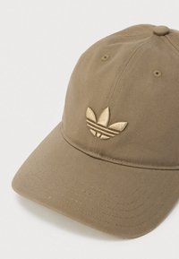 Light brown baseball cap with embroidered Adidas trefoil logo on front, featuring stitched ventilation holes and curved brim.