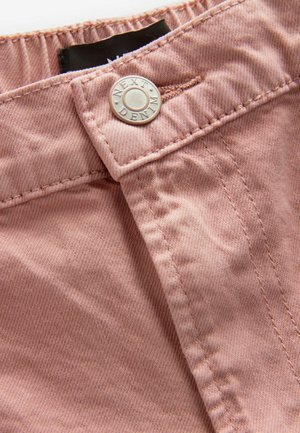 Tissu en denim rose avec une texture fine, comportant un bouton-pression argenté portant l'inscription "NEXT", et des coutures soignées le long des bords.