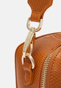 Brun texturerad läderväska med en detaljerad lås och dragkedja i guldton, formad med rundade kanter och en slät yta.